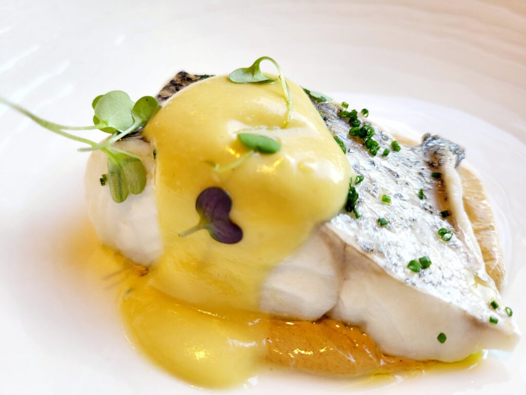  Acerccamiento de un plato con un  trozo de Bacalao al pil pil con unos pequeños brotes encima